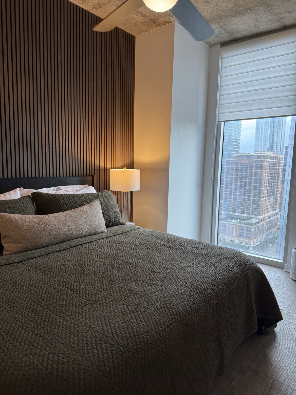 Bedroom with a vertical wood slat accent wall, dark bedding and a city view, by Refinery ATX in Austin, TX