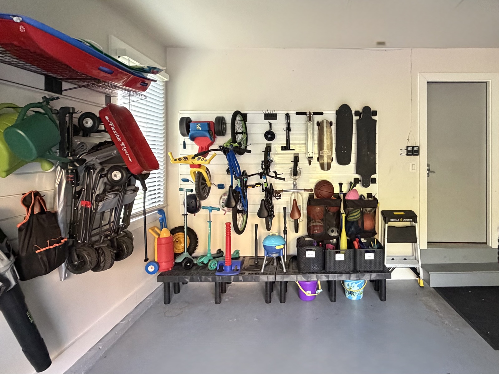 Garage wall with bikes, scooters and skateboards hung on a slat wall above a bench of labeled bins, organized by Refinery ATX in Austin, TX