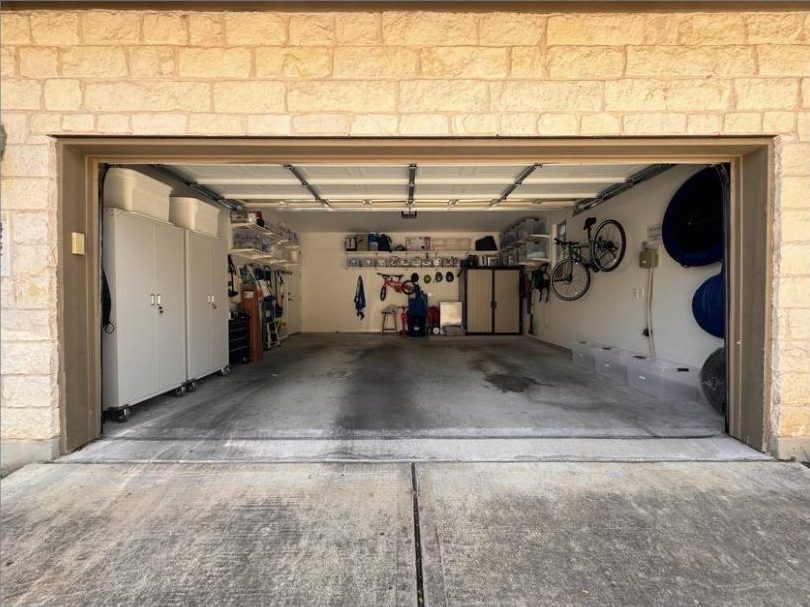 Two-car garage with white cabinetry along one wall, bikes hung overhead and a clear swept floor, in Austin, TX