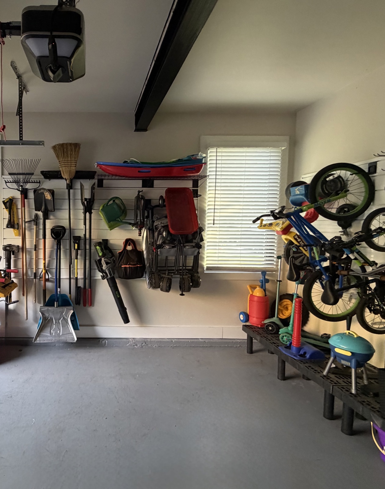 Garage wall with rakes, shovels and yard tools hung on a slat wall, a folding wagon and kids' bikes stored off the floor, in Austin, TX