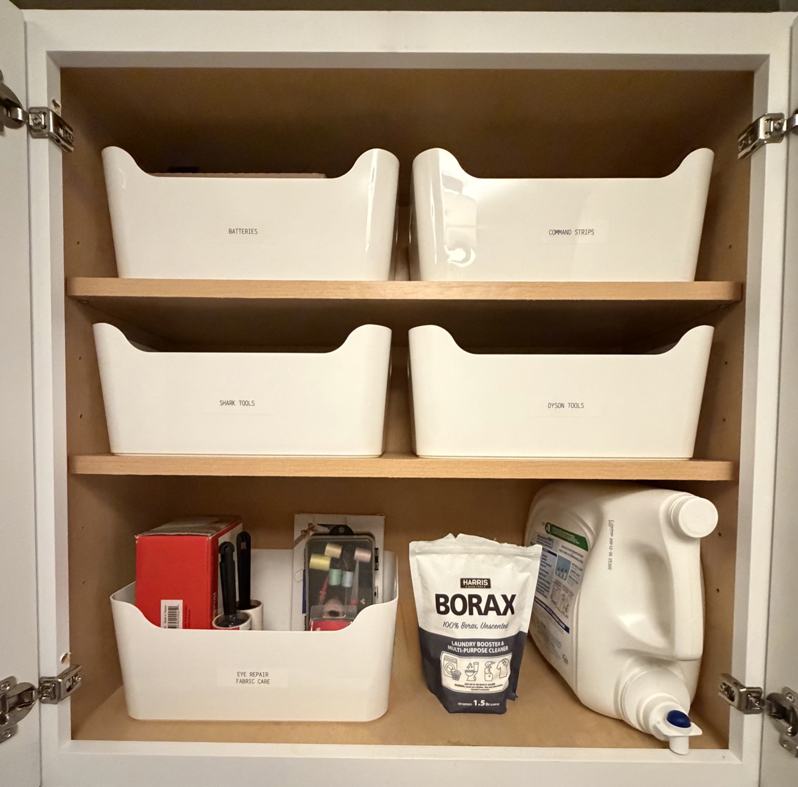 Laundry cabinet with labeled white bins for batteries, command strips, vacuum tools and fabric care beside detergent and borax, organized by Refinery ATX in Austin, TX