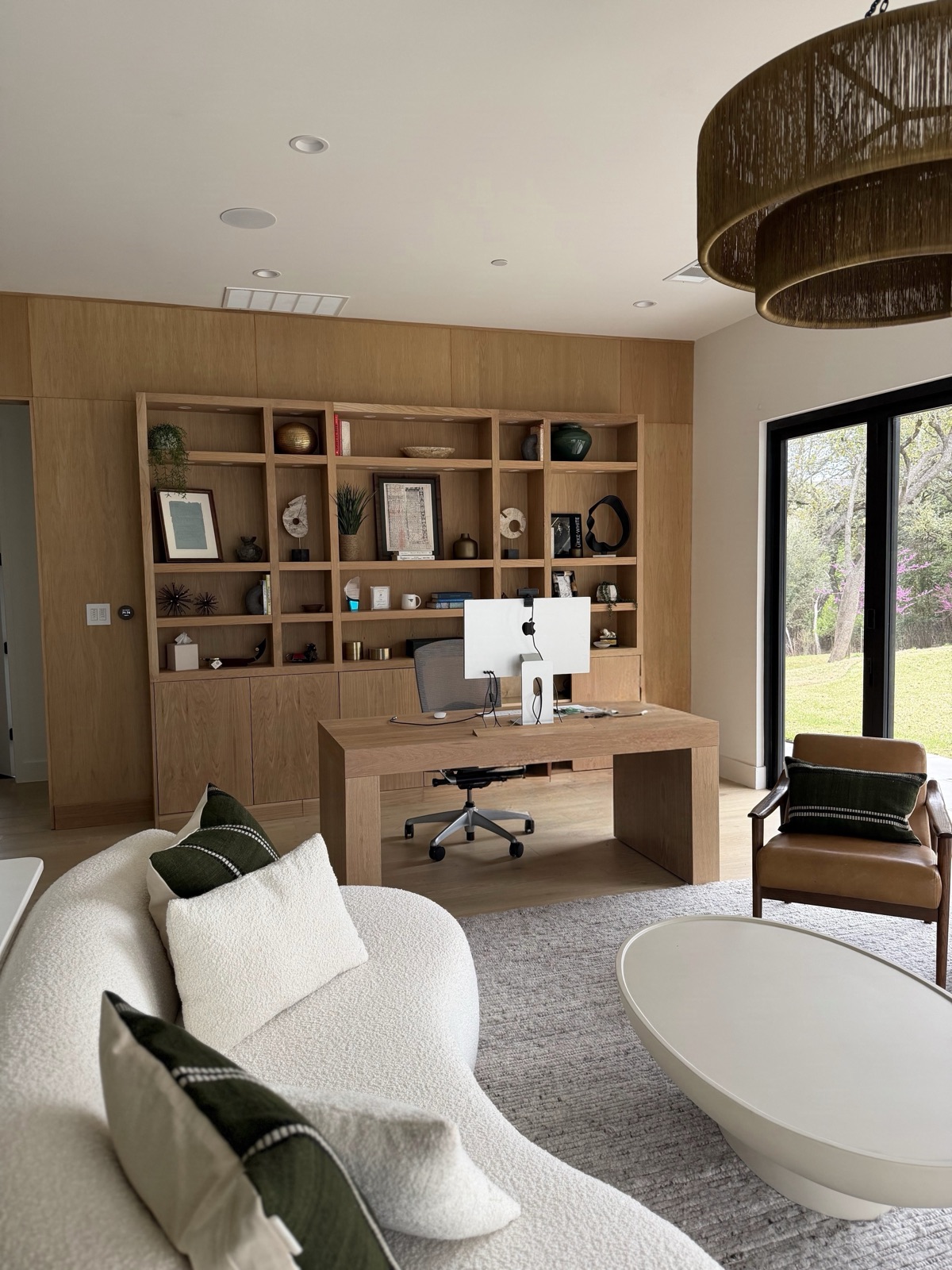 Living room and home office with custom white oak built-ins, a desk and a curved sofa, by Refinery ATX in Austin, TX