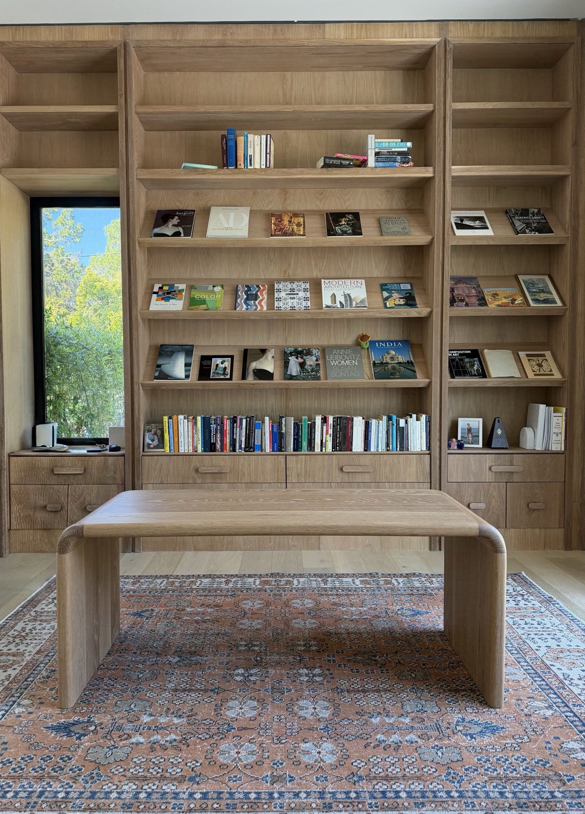 Floor-to-ceiling white oak library shelving with a long reading table and patterned rug, by Refinery ATX in Austin, TX