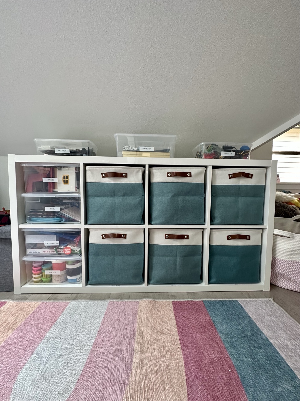 Built-in cubbies fitted with teal fabric bins and clear drawers for toys and craft supplies, on a striped rug
